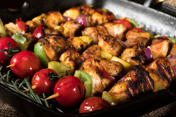 Grilled chicken skewers with spices and vegetables in a pan