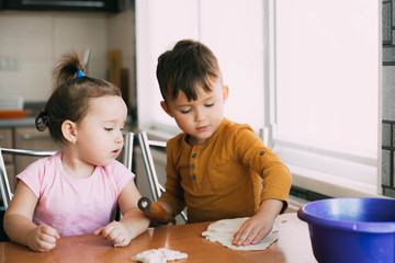 Children, brother and sister during the day in the kitchen prepare pastry or pizza or pie
