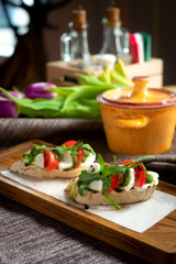Bruschetta with tomatoes, mozzarella cheese and rocket on a old wooden board. Traditional italian appetizer or antipasto