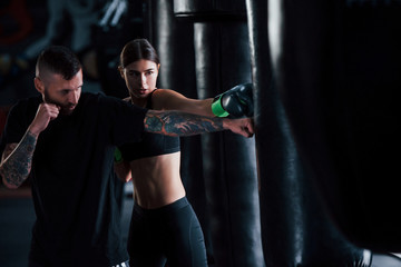 Young tattooed boxing coach teaches young woman in the gym