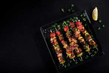 Grilled chicken skewers with spices and vegetables on plate and black background