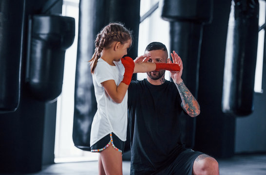 Basic punches. Young tattooed boxing coach teaches cute little girl in the gym