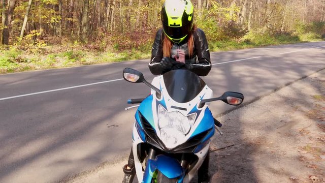 The girl in a black leather suit starts a motorcycle. Getting started. Riding. Racer. Neon helmet. Sport motorcycle. Autumn forest. Travel.