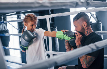 Having sparring with each other on the boxing ring. Young tattooed boxing coach teaches cute little...