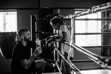 Fototapeta na wymiar Conception of assistance. Young tattooed boxing coach teaches cute little girl in the gym