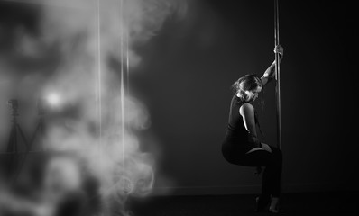 The dancer on the pylon in the studio. Girl doing exercises on a sports equipment.