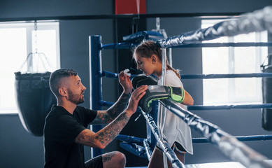 Conception of assistance. Young tattooed boxing coach teaches cute little girl in the gym