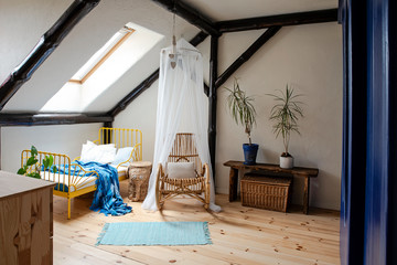 Interior of room in the attic with space and wooden floow. Yellow bed and blue throw in modern design. Minimalism and simplicity in child's room in apartment.