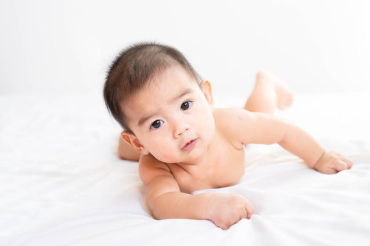 A little asian baby boy is trying to clawn on the bed in the morning time, concept of healthy care and child development in the first year old.