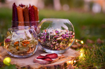 Collection of healing herbs in a glass bowl. Dry petals of tea rose and linden tree flowers. Alternative medicine, herbal treatments. Photo taken on a background of a summer forest.