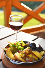 A dish of national Ukrainian cuisine and a glass of wine on a table overlooking a green lawn. Fried potatoes and homemade black pudding.