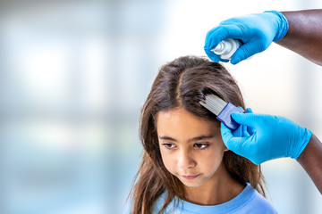 Mother treating daughter's hair against lice ith spray treament