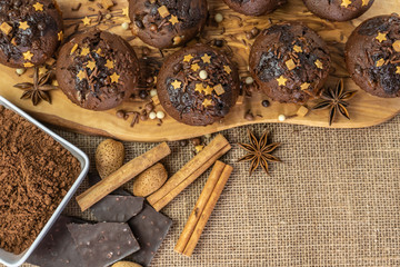 Chocolate holiday cupcakes, muffins with cake sprinkles on a wooden board, chocolate, cinnamon sticks, star anise, cocoa, nuts, burlap sack