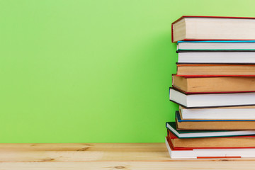 Simple composition of many hardback books, raw of books on wooden table and light green background