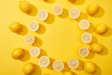 top view of ripe cut and whole lemons arranged in round frame on yellow background with copy space