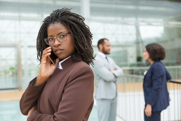 Serious pensive professional talking on mobile phone, looking at camera. Her male and female...