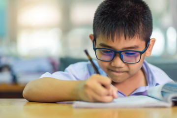 Asian elementary school boy in a white school uniform and wearing glasses, is studying in the classroom.