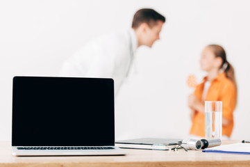 selective focus of pediatrist and child and laptop with blank screen on foreground