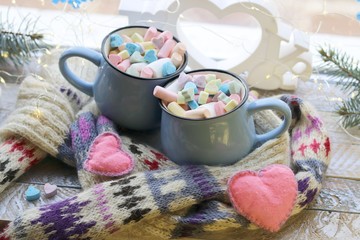 A pair of cups with a drink decorated with meringues and marshmallows, Christmas decor, hearts, knitted scarf on the windowsill, home comfort concept, winter holidays