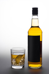 Bottle and glass of whiskey with ice on a white-gray background