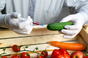 A man injects chemicals into a cucumber, fertilizers and chemicals with a syringe to increase the shelf life of vegetables. Chemical processing of vegetables, injection with chemicals.