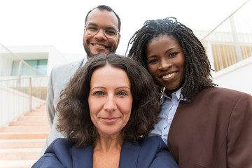 Fototapeta premium Happy successful business team taking selfie outside. Self portrait of business man and women standing near office building, smiling. Unity or teamwork concept