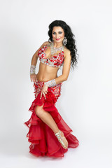 Girl in a red dress for oriental dancing. Brunette in beautiful long red dress to perform belly dance on a white background