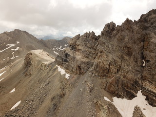 vue aérienne de sommet de haute montagne rocailleux avec strates géologiques et neiges éternelles par temps nuageux avec percée de soleil