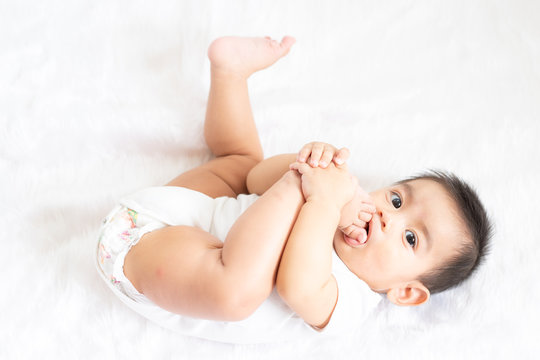 A cute 6 months old asian little baby boy is playing his hands and feet with fully happiness moment on the bed in the morning time, concept of healthy and child development in the first year of life.