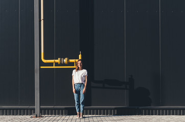Beautiful Woman in white shirt and jeans against black wall and yellow gas pipe