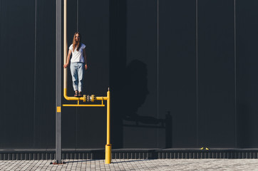 Beautiful Woman in white shirt and jeans standing on yellow gas pipe near black wall