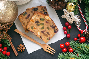 Sweet fruit cake slices on white paper put on black granite table in top view flat lay with Christmas decoration. Traditional rum fruit cake for Christmas celebrate festival. Homemade bakery concept.