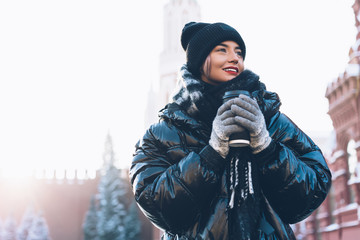 Smiling female in cozy jacket with hot beverage.