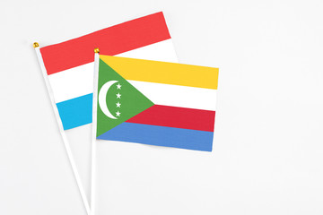 Comoros and Luxembourg stick flags on white background. High quality fabric, miniature national flag. Peaceful global concept.White floor for copy space.
