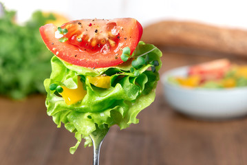 Bright juicy vegetables on a fork on the background of the table. A slice of tomato with spices, lettuce and yellow pepper on a fork. Mixed salad, diet and vegan dishes.