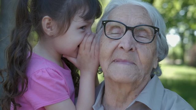 Secret for grandma. A little girl tells her secrets in her grandmother's ear.