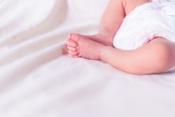 Fototapeta na wymiar Close-up of newborn baby girl's tiny legs and feet, selective focus photograph.