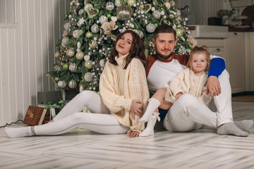 Beautiful young family sitting next to a nicely decorated Christmas tree. Happy family having fun with Christmas presents at home. Christmas at home by the fireplace and the Christmas tree. Portrait