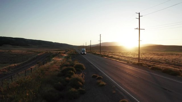 Semi truck driving toward camera on highway in golden sunrise landscape