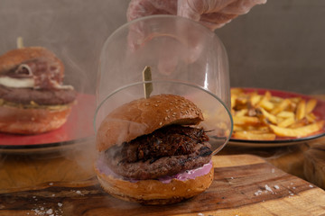 Close-up of chef's hand lifting a glass bowl of delicious homemade smoked hunger with wood chips...