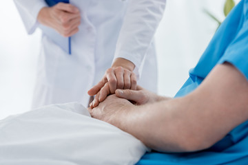 cropped view of doctor in white coat holding hand of patient in hospital