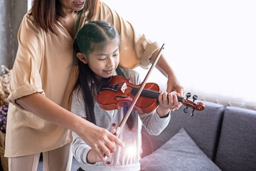 Teacher teaching little girl for playing violin music class,at studio music room,with happy...
