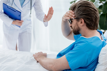 cropped view of doctor in white coat calming down sad patient in hospital