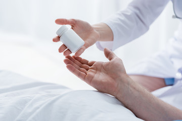Fototapeta premium cropped view of doctor giving bottle with pills to patient in hospital