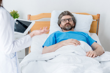 cropped view of doctor holding digital tablet and patient lying in bed in hospital