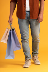 cropped view of man standing with shopping bags on orange