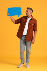 handsome man holding blue speech bubble and standing on orange