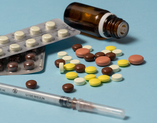 syringe and various medications, vitamins pills laid out on a blue background.