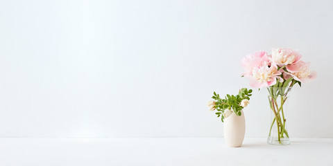 Home interior with decor elements. Pink peonies in a vase and white flowers on a white background