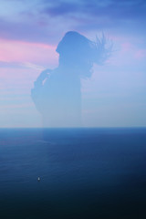 Silhouette of a girl with flying hair on a background of blue sea and sails double exposure